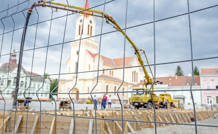 View on the pump crane for lifting and casting concrete at construction site through a fence wire with quadratic shape.